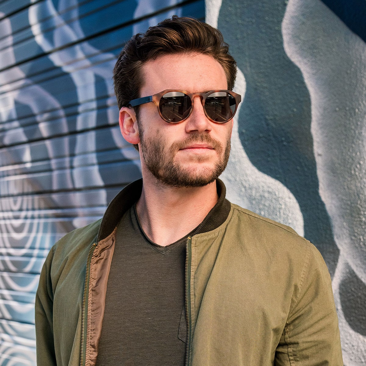 distil cooper sunglasses on bearded man wearing green bomber jacket in alley